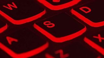 A computer keyboard shows several letters. It is black and backlit with red light.