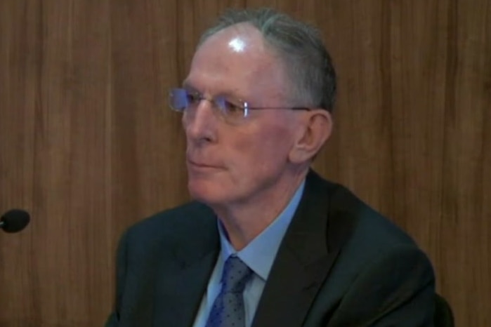 Tony Biggin sits in a chair wearing a suit.