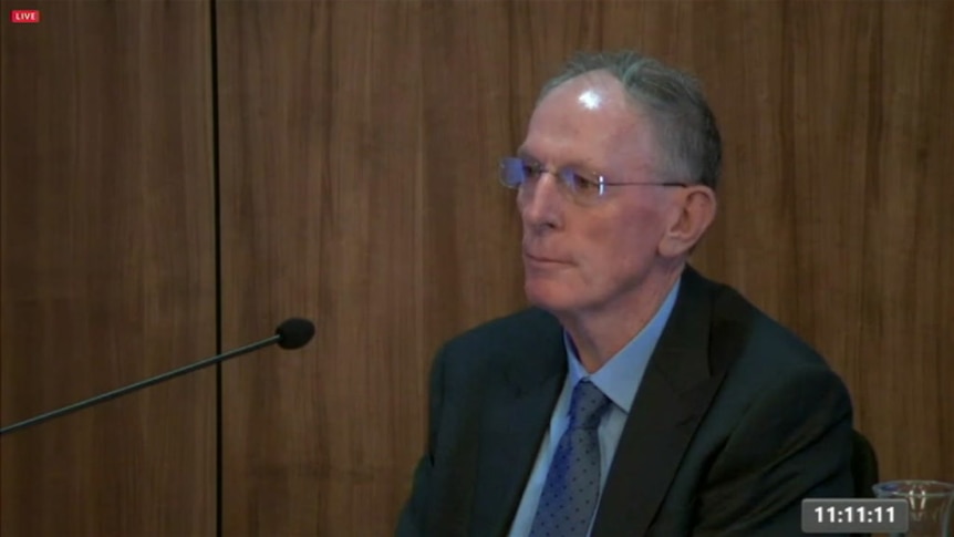 Tony Biggin sits in a chair wearing a suit.