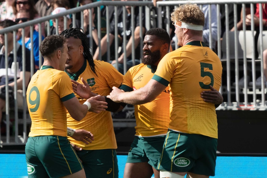 Four Australian Wallabies players celebrate a try against New Zealand's All Blacks.