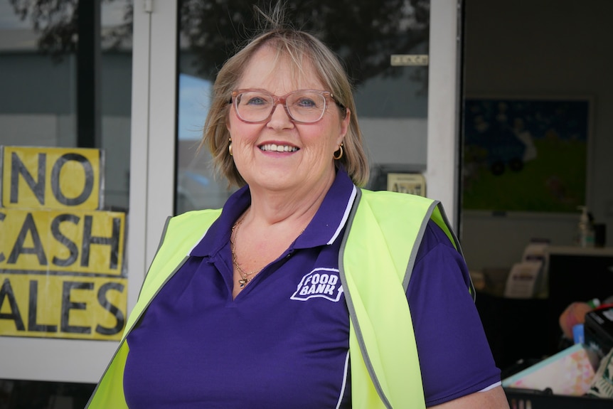 Lady wearing a purple T-shirt and high vis, standing in front of a Foodbank warehouse. 