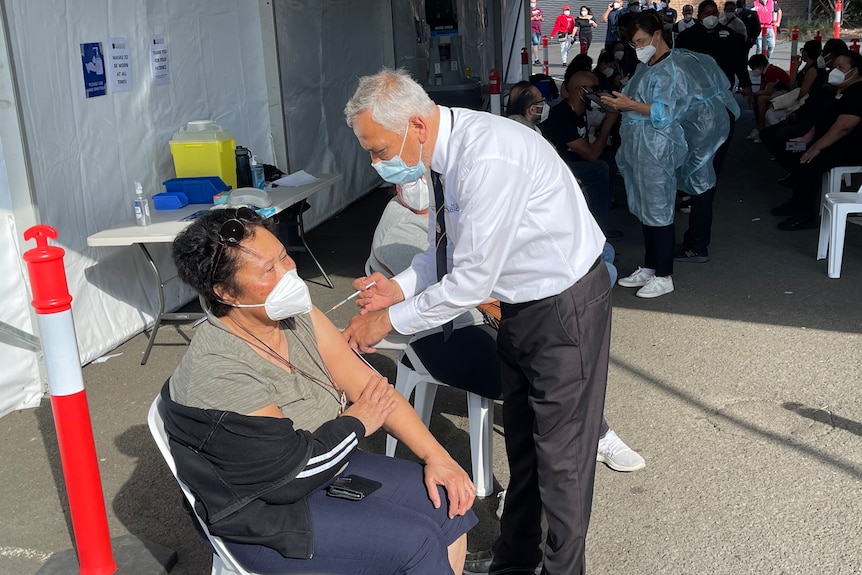 masked man holds needle to elderly woman's arm