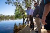 Three men standing next to a river with one pointing