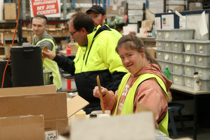 A young woman in high-vis stirring with a wooden spoon inside a warehouse.