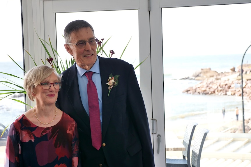 The couple stand smiling in their wedding gear