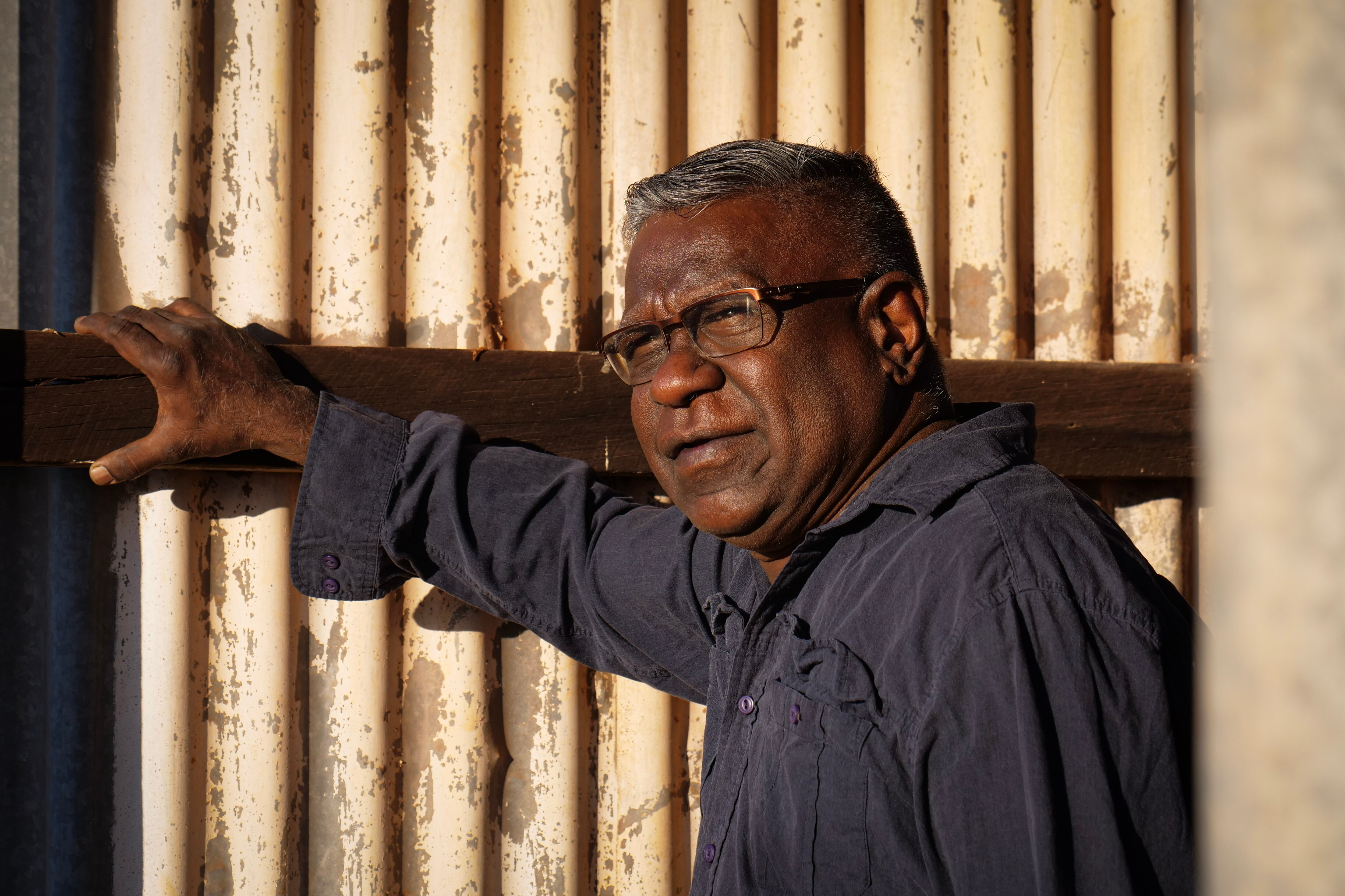 Un aborigen de mediana edad se apoya en la estructura de un edificio abandonado.