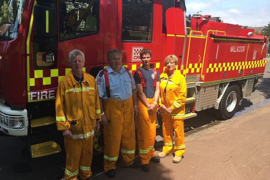 Three men and one woman in firefighting uniforms in front of a fire truck with "Mallacoota" written on it.