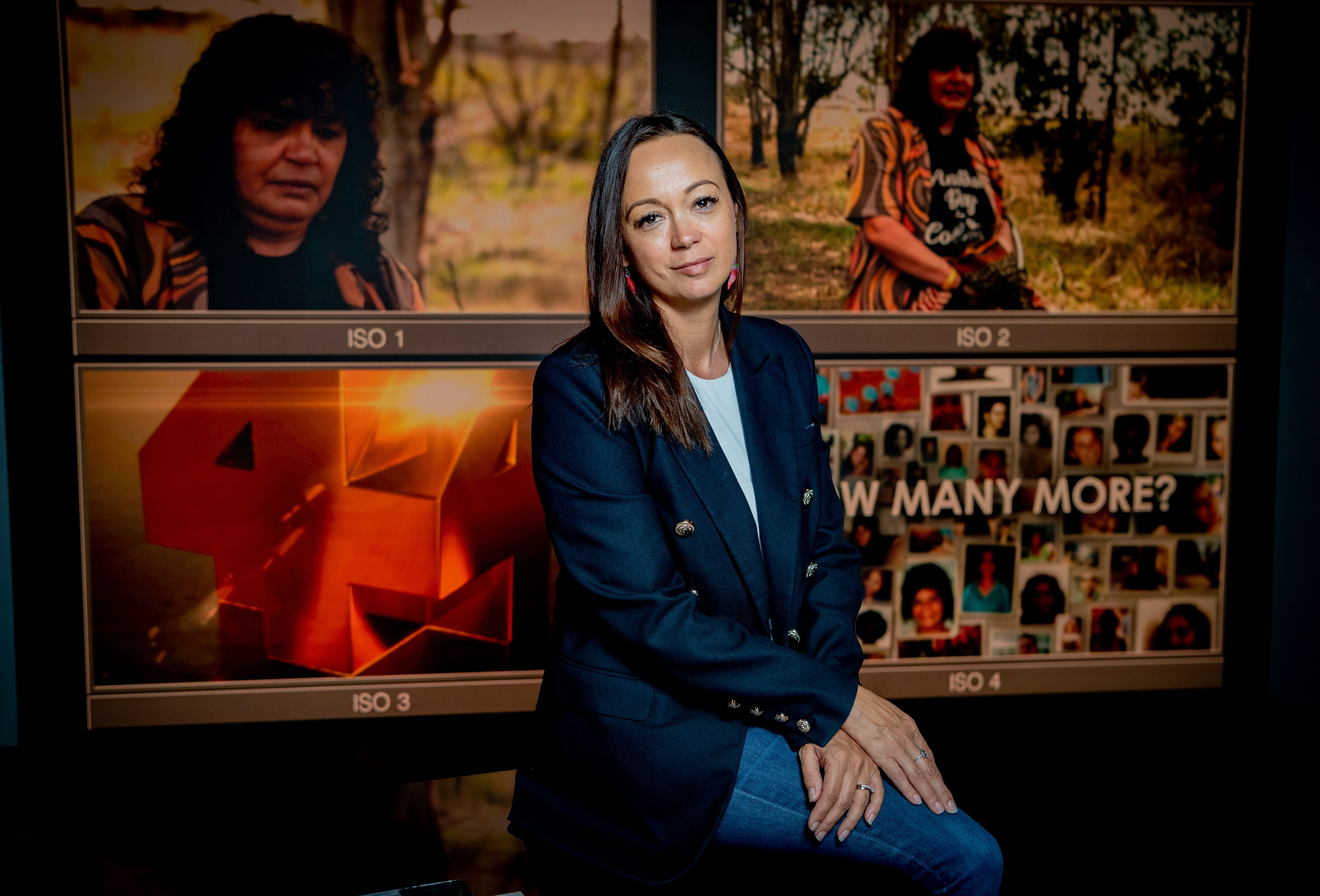 Woman sitting in front of TV screens showing Four Corners logo and images from program on deaths of Indigenous women.