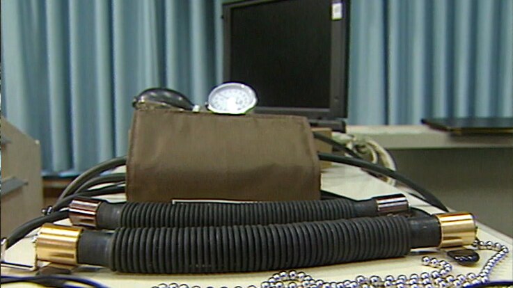 Wires, a silver balled chain, a blood pressure monitor and a laptop computer laid out on a table.
