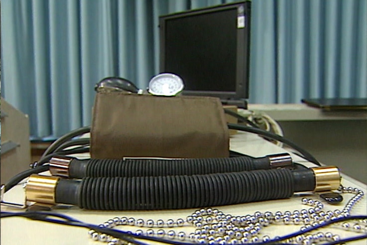 Wires, a silver balled chain, a blood pressure monitor and a laptop computer laid out on a table.