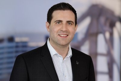 A smiling man with neat, dark hair, wearing a dark suit.