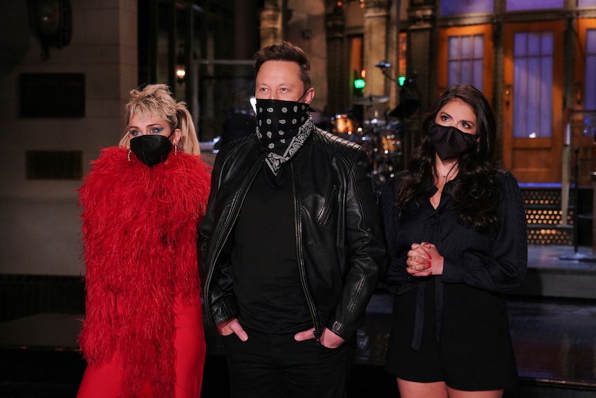 Miley Cyrus, Elon Musk and Cecily Strong on a tv studio stage wearing masks