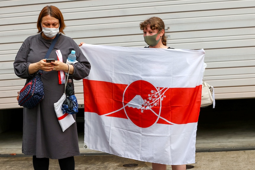 A woman wearing a face mask holds a white and red flag. 