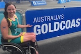 Para-traithlete Emily Tapp sitting in front of a large sign reading Gold Coast.