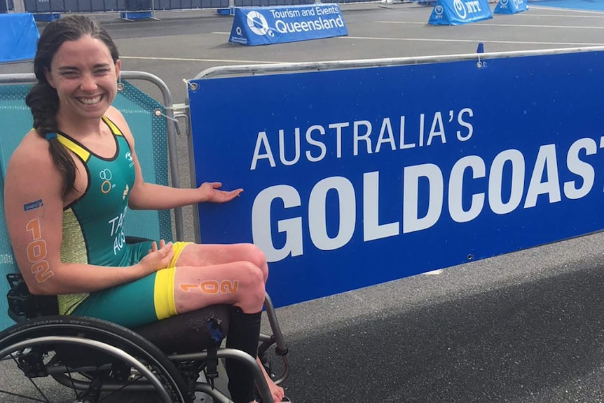 Para-traithlete Emily Tapp sitting in front of a large sign reading Gold Coast.