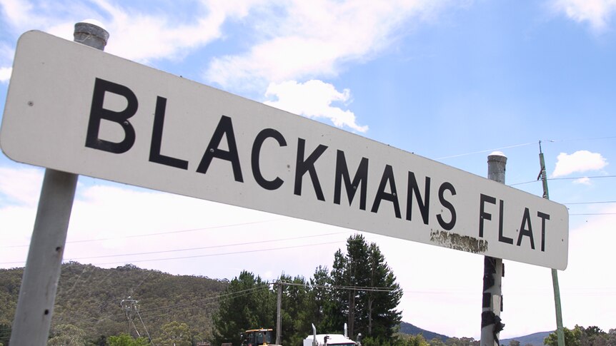 Road sign of Blackmans Flat with a big truck driving past carrying a digger