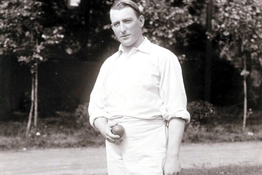 A black and white photo of Warwick Armstrong in whites and holding a cricket ball, signed "yours sincerely, Warwick Armstrong"