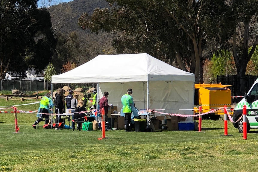 A marquee white tent stands on a grassy oval, people in high-vis and others gathered there.