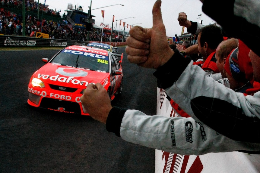 A Ford team worker gives a big thumbs up as a car drives past on the finishing straight after winning the Bathurst 1000.