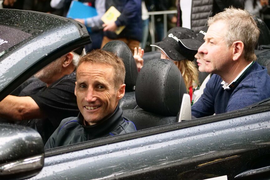 Jockey Damien Oliver sits in a soft top car with the roof down in the rain at the Melbourne Cup parade.