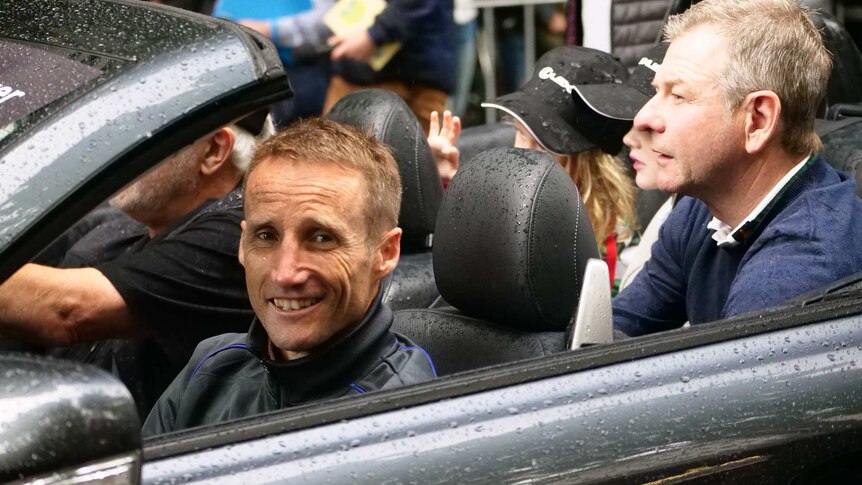 Jockey Damien Oliver sits in a soft top car with the roof down in the rain at the Melbourne Cup parade.