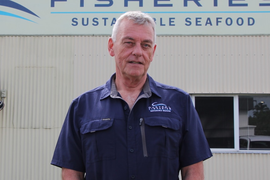 a man stands in front of a tin seafood company building in a dark blue button up