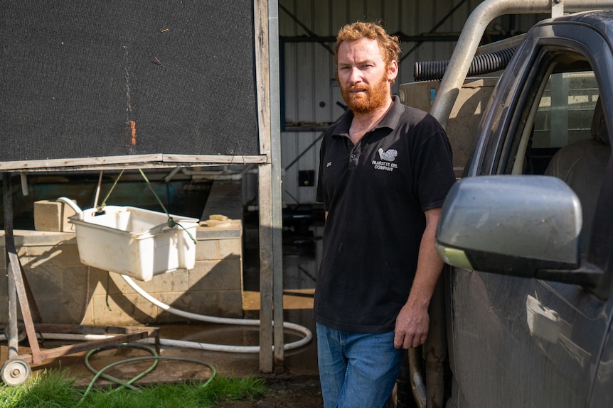 A man with red hair and beard stands next to his ute.