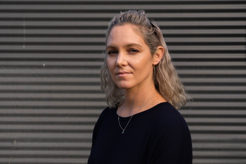 A picture of Australian National University domestic, family and sexual violence researcher Chay Brown in front of a grey wall.