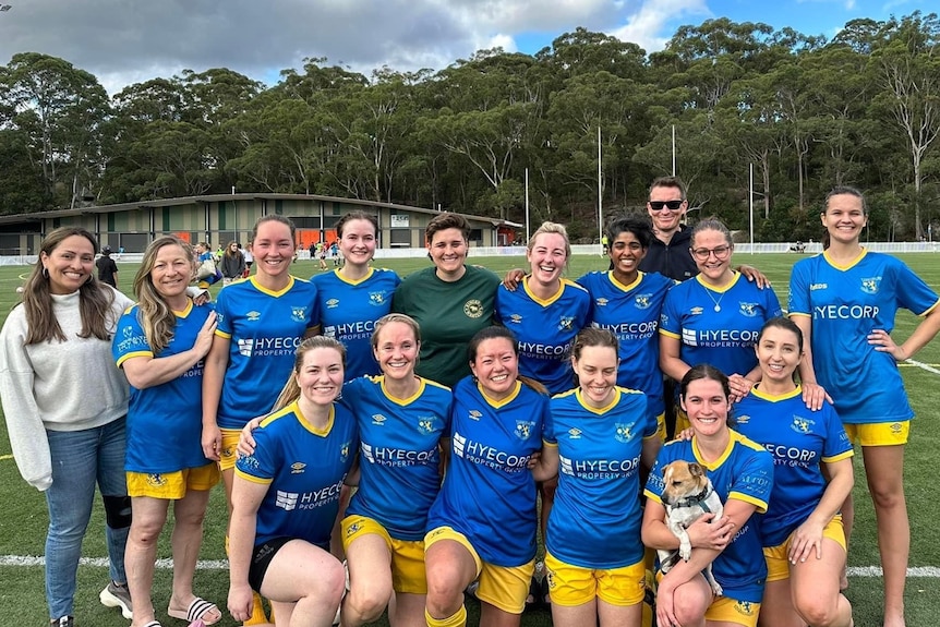A suburban womens soccer team smile in their uniforms, sweaty after a match.