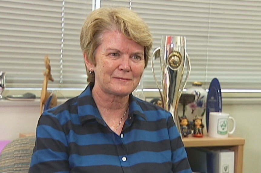 Heather Reid sits at her desk in front of a cabinet full of trophies and memorabilia.