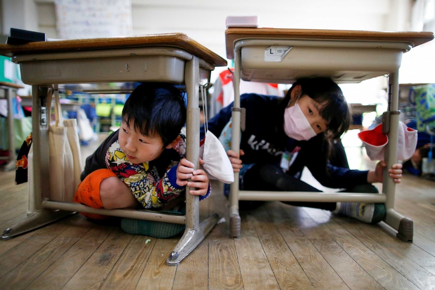 Two little kids sit under their school desks in Japan