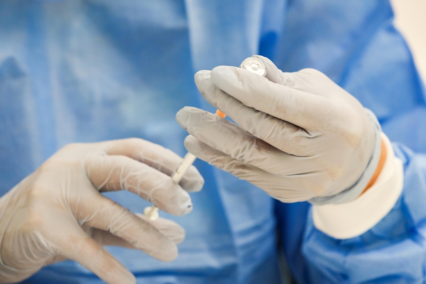 A nurse holding a needle and a vial.