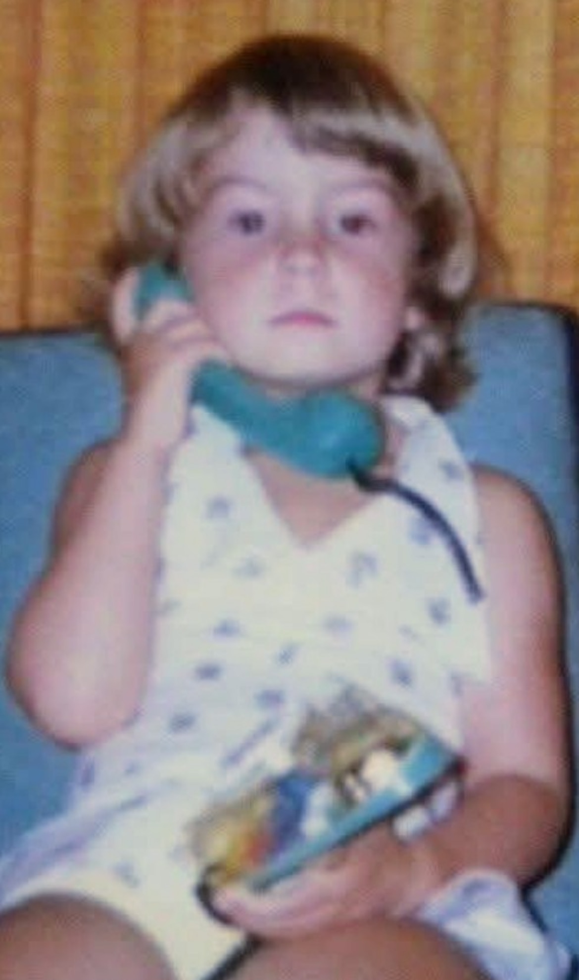 A child looks at the camera while holding the phone to his ear.