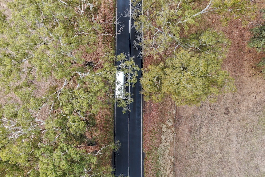 An aerial photo of a white mini bus travelling along a country road.