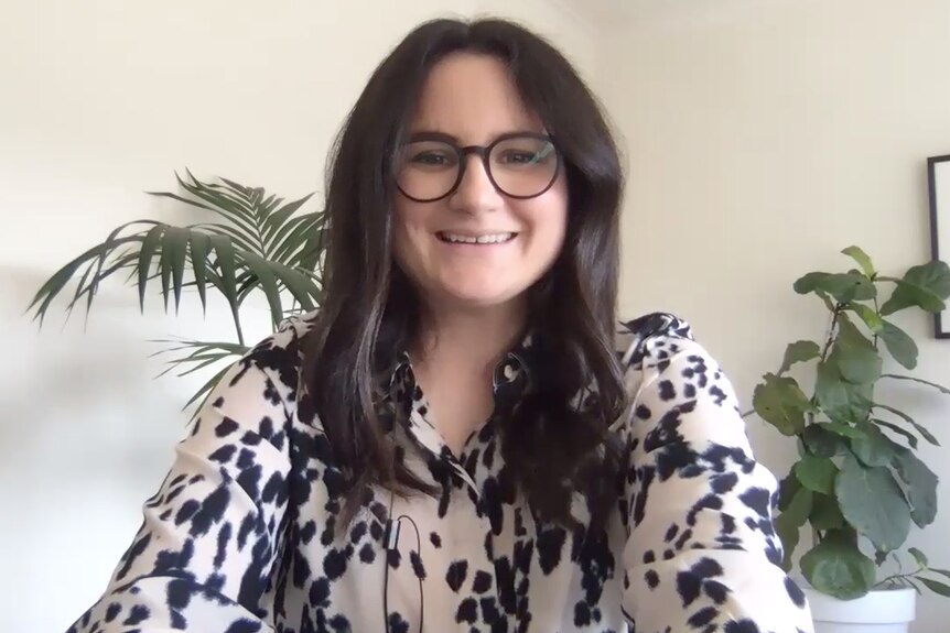 Dr Christine Grové, a white woman with long brown hair and glasses smiles in her home.