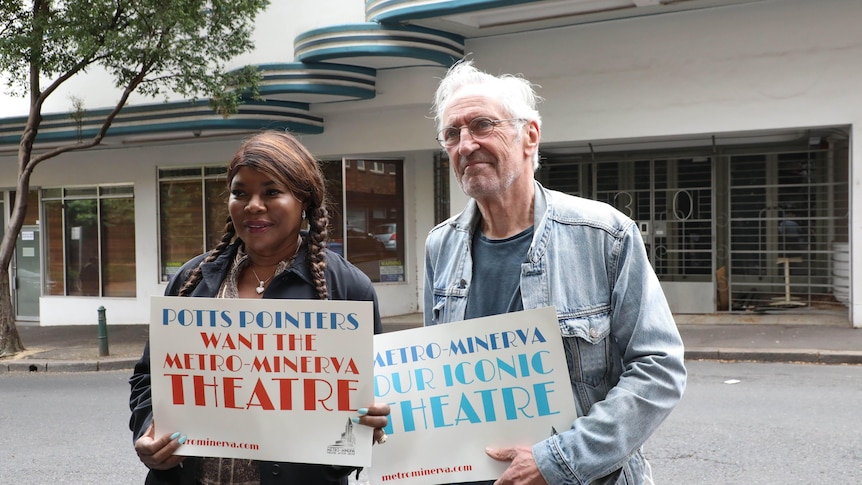 Marcia Hines and John Waters stand in front of a building with posters saying it should be a theatre