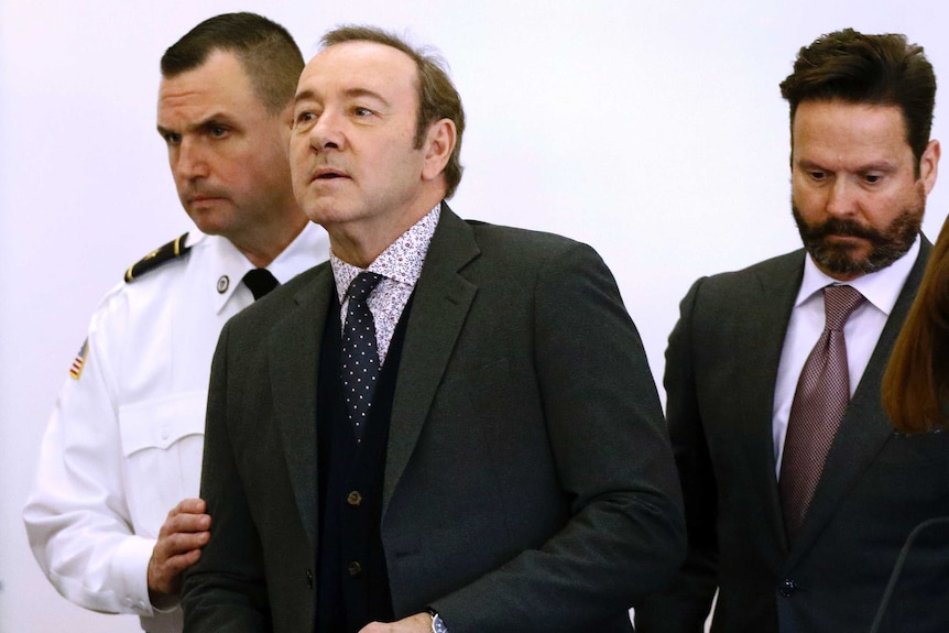 Actor Kevin Spacey enters the courtroom accompanied by a uniformed guard.