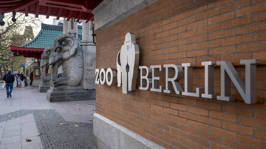 A sign saying Zoo Berlin on a brick wall, with statues of elephants in the background. 