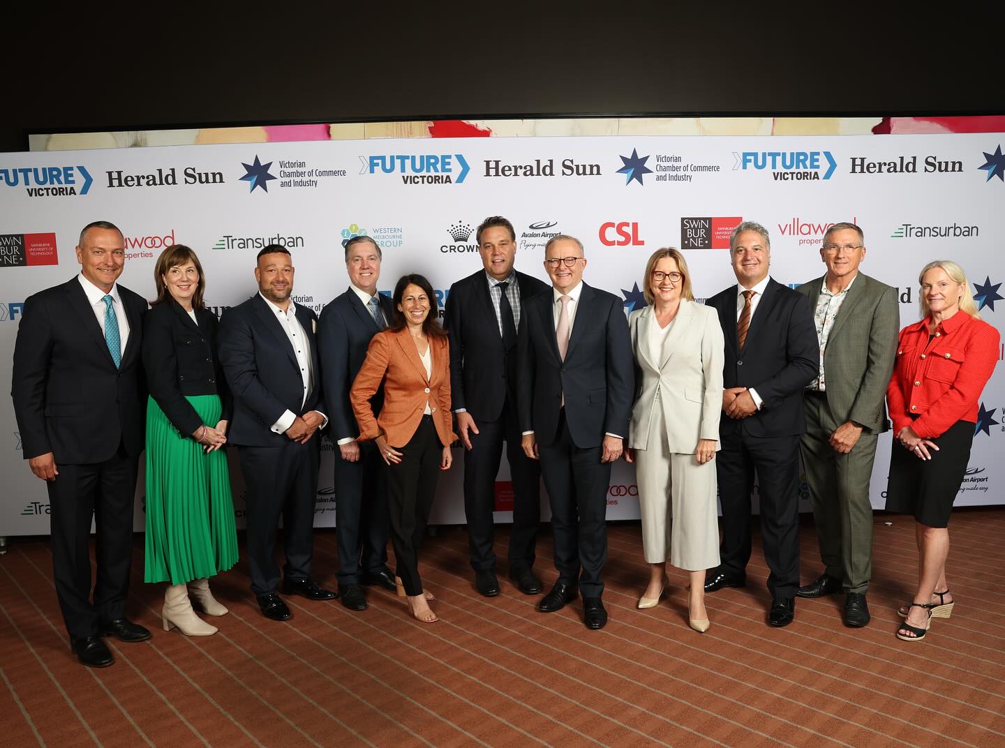 A group of men and women stand together for a photo in front of a board advertising companies and media outlets.