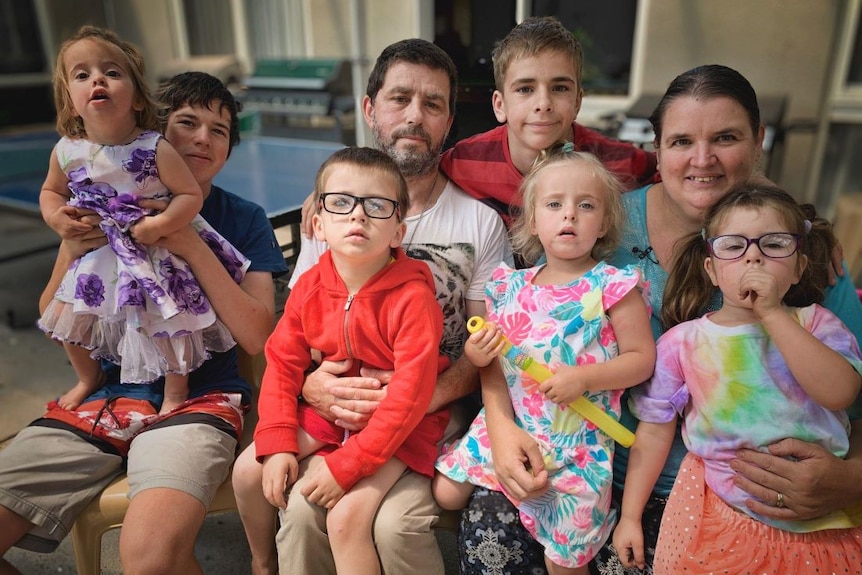 A family including six children, pose for a photo with their arms around each other.