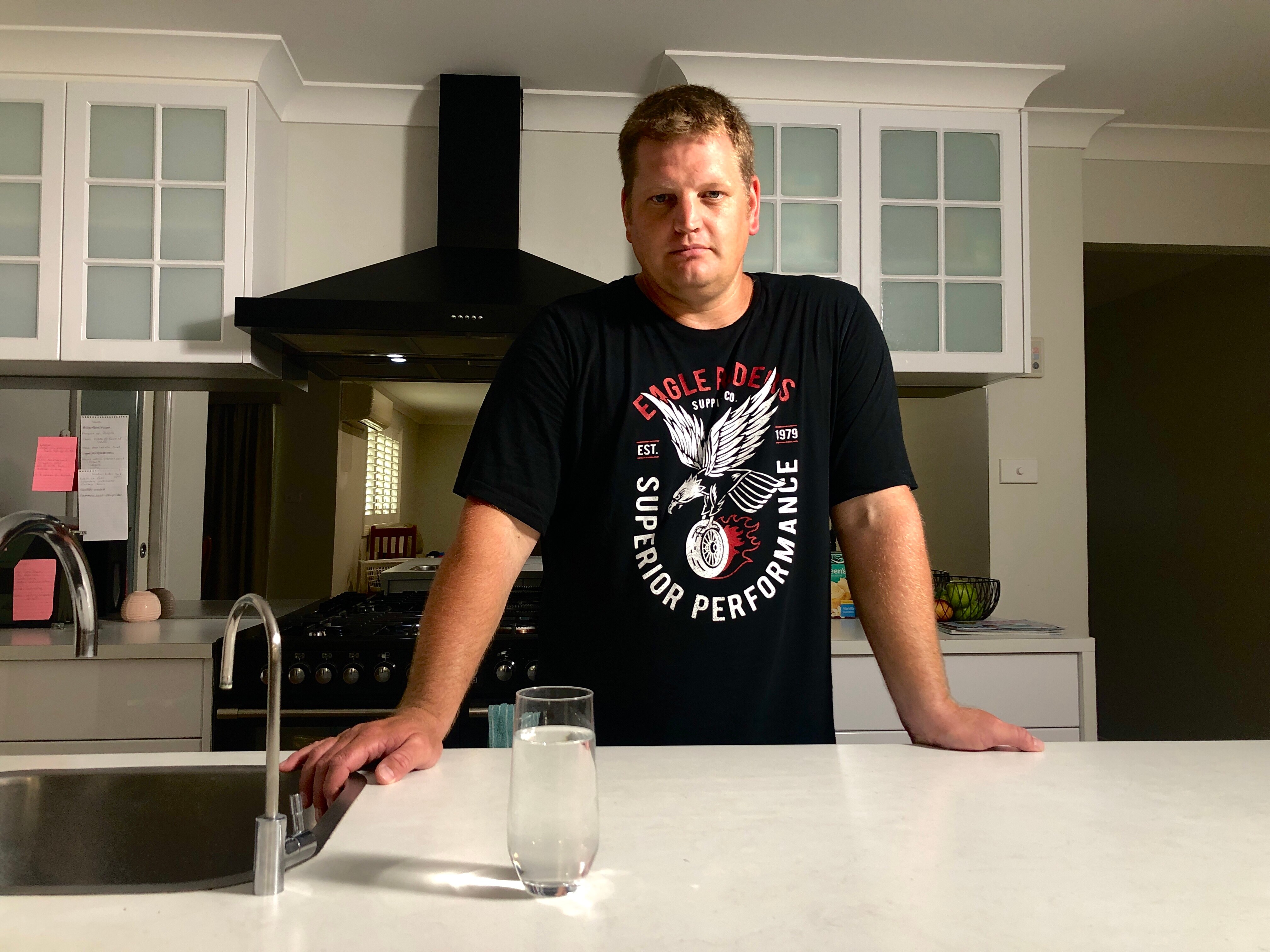 A man leaning on a bench with a glass of water in front of him. 
