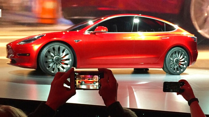 A red car on a stage in front of a crowd taking photos on their smart phones.