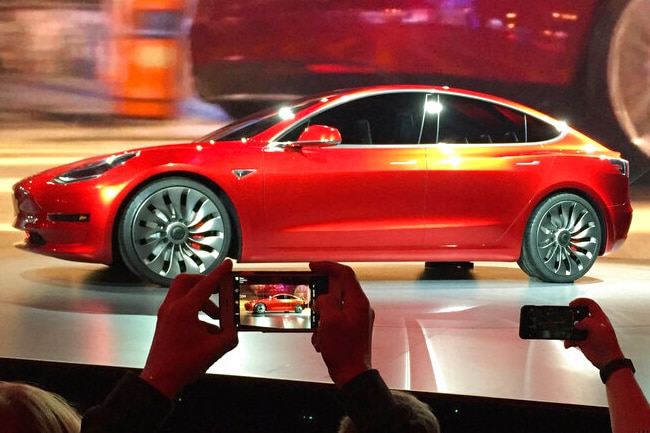 A red car on a stage in front of a crowd taking photos on their smart phones.