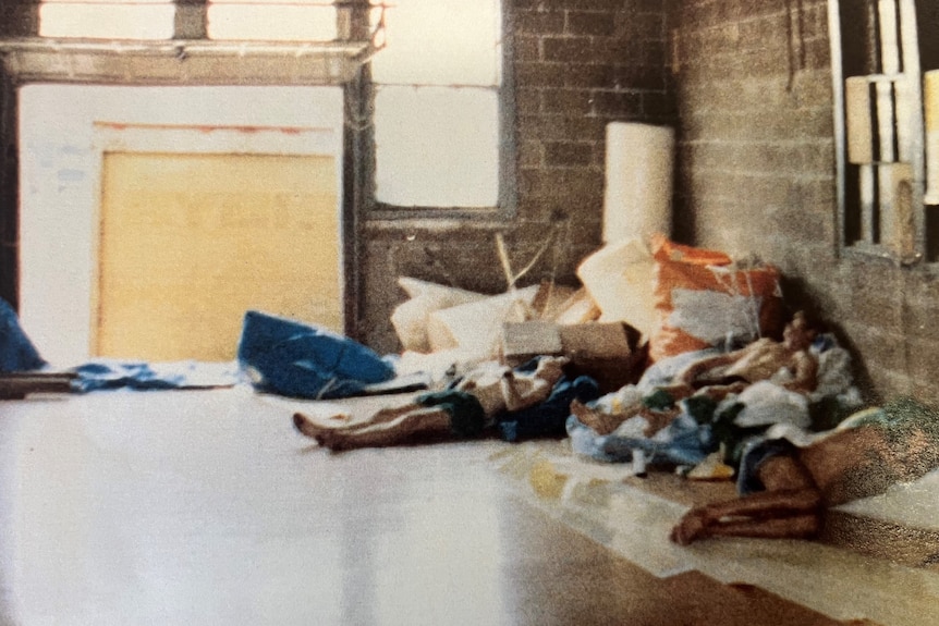 An old grainy photo of three men lying down on lots of pieces of material in what was known as the sail loft.