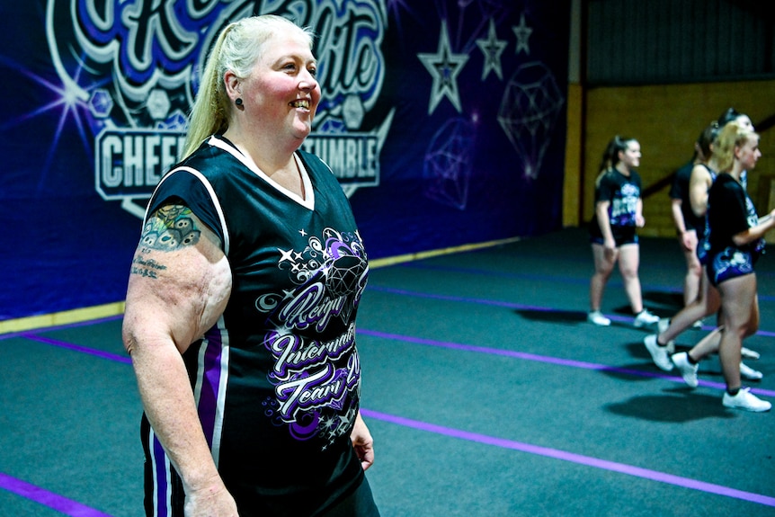 A woman walks on a gym mat and smiles.