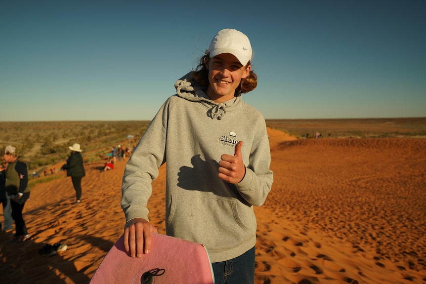 Boy in grey hoodie and white cap on sand dune