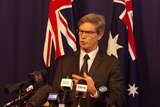 Mike Nahan speaking in front of microphones with Australian flags in the background.