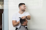 A barber cuts a man's hair. 