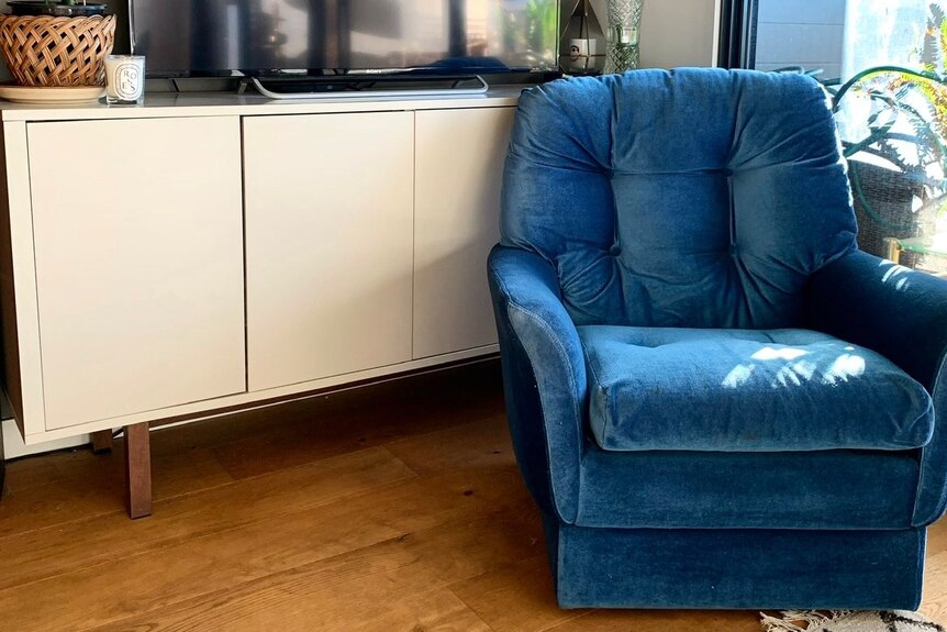 A blue velvet chair sits in front of a TV cabinet