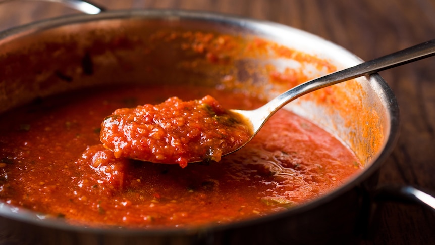 A spoonful of tomato pasta sauce from a pot.